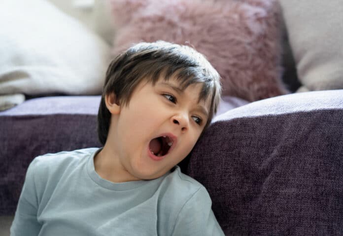 Authentic tired kid yawning sitting next to sofa