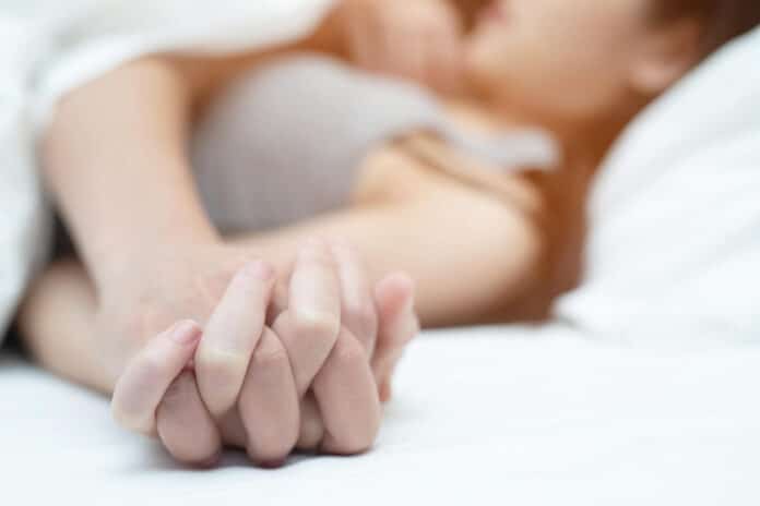 couples holding hands while lying on bed