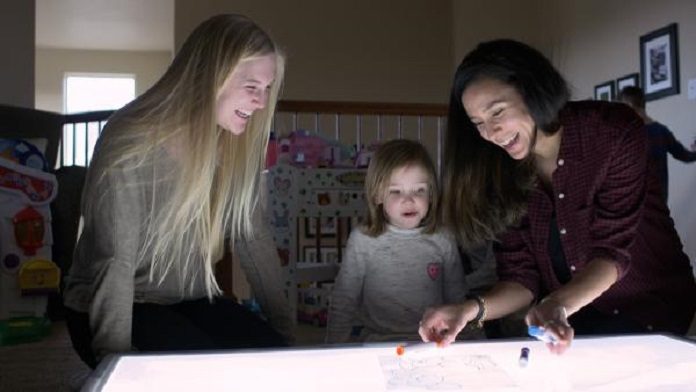 Undergraduate research associate Allie Coy (left) and CU Boulder instructor Lameese Akacem (right) play with a child over a light table.