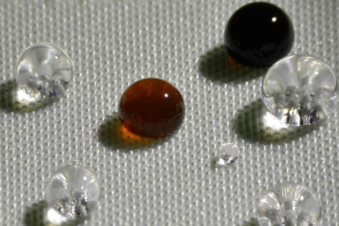 Repellency of different liquids on polyester fabric coated with H1F7Ma-co-DVB: soy sauce (black drop), coffee (brown drop), HCl acid (top left transparent drop), NaOH (bottom right transparent drop) and water (remaining transparent drops). Image: Varanasi and Gleason research groups