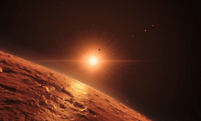 This artist’s impression shows the view just above the surface of one of the middle planets in the TRAPPIST-1 system, with the glare of the host star illuminating the rocky surface. At least seven planets orbit this ultracool dwarf star 40 light-years from Earth and they are all roughly the same size as the Earth. They are at the right distances from their star for liquid water to exist on the surfaces of several of them. This artist’s impression is based on the known physical parameters for the planets and stars seen, and uses a vast database of objects in the Universe. Credit: ESO/N. Bartmann