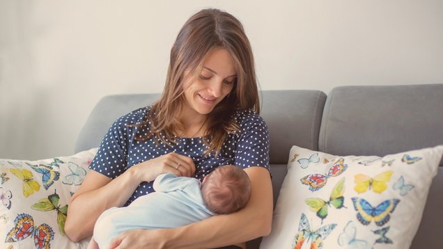 Young mother breastfeeding her newborn baby boy at home