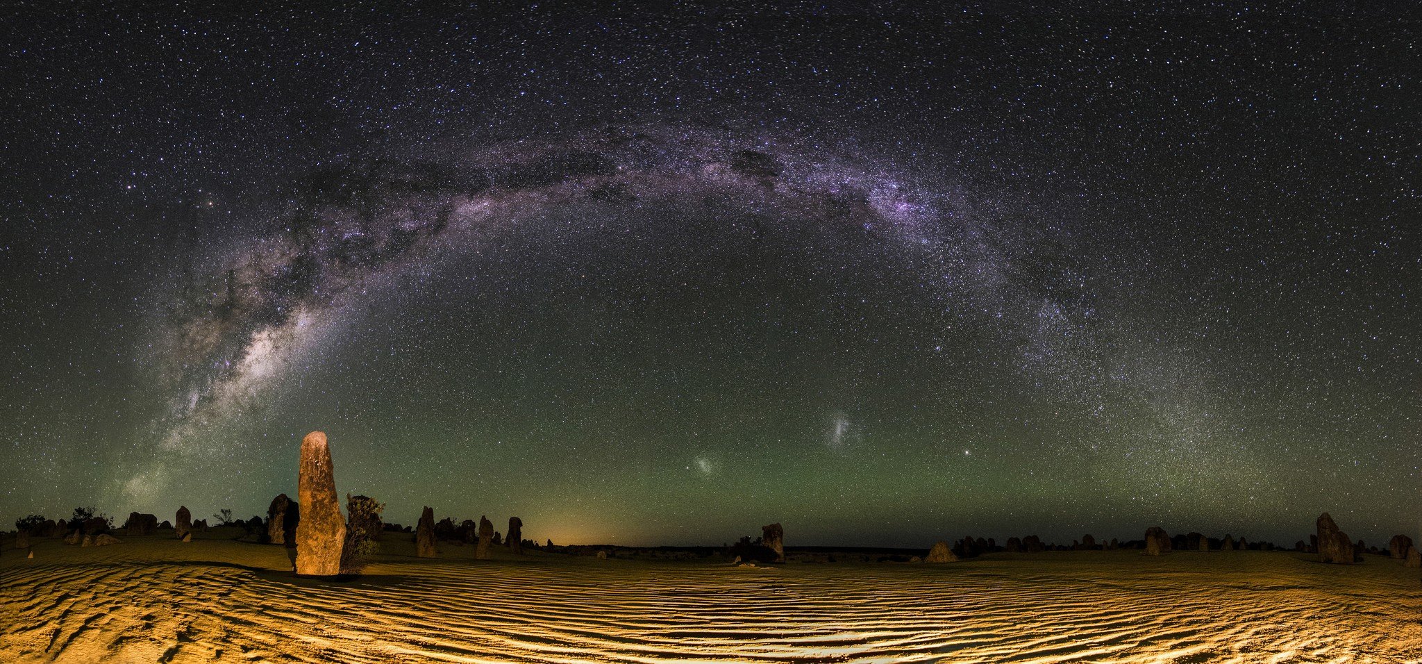 The Milky Way arching over the Large and Small Magellanic Clouds as viewed from the Pinnacles Desert in Western Australia. Credit: inefekt69 / Flickr.