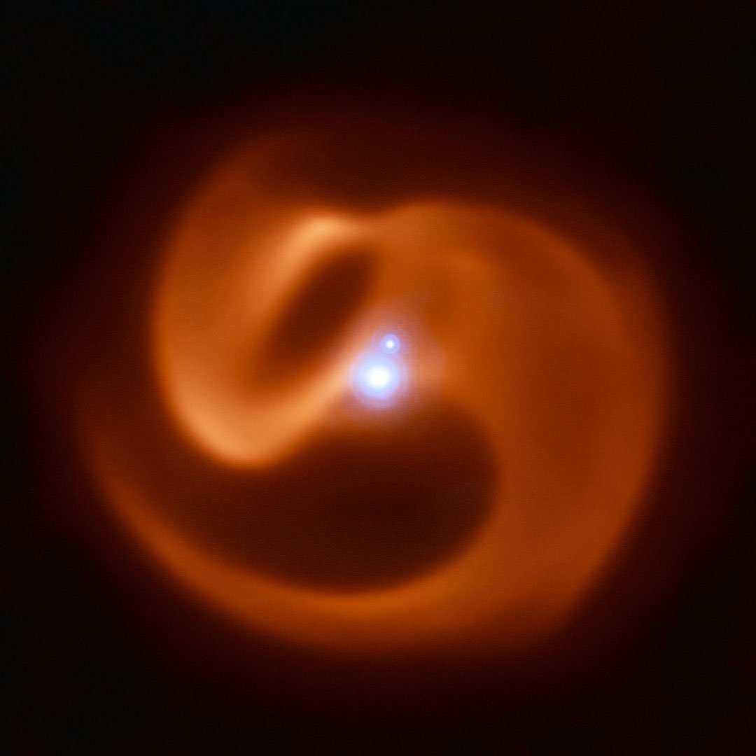 The VISIR instrument on ESO’s VLT captured this stunning image of a newly-discovered massive binary star system. Nicknamed Apep after an ancient Egyptian deity, it could be the first gamma-ray burst progenitor to be found in our galaxy. Apep’s stellar winds have created the dust cloud surrounding the system, which consists of a binary star with a fainter companion. With 2 Wolf-Rayet stars orbiting each other in the binary, the serpentine swirls surrounding Apep are formed by the collision of two sets of powerful stellar winds, which create the spectacular dust plumes seen in the image. The reddish pinwheel in this image is data from the VISIR instrument on ESO’s Very Large Telescope (VLT), and shows the spectacular plumes of dust surrounding Apep. The blue sources at the centre of the image are a triple star system — which consists of a binary star system and a companion single star bound together by gravity. Though only two star-like objects are visible in the image, the lower source is in fact an unresolved binary Wolf-Rayet star. The triple star system was captured by the NACOadaptive optics instrument on the VLT. Credit:ESO/Callingham et al.
