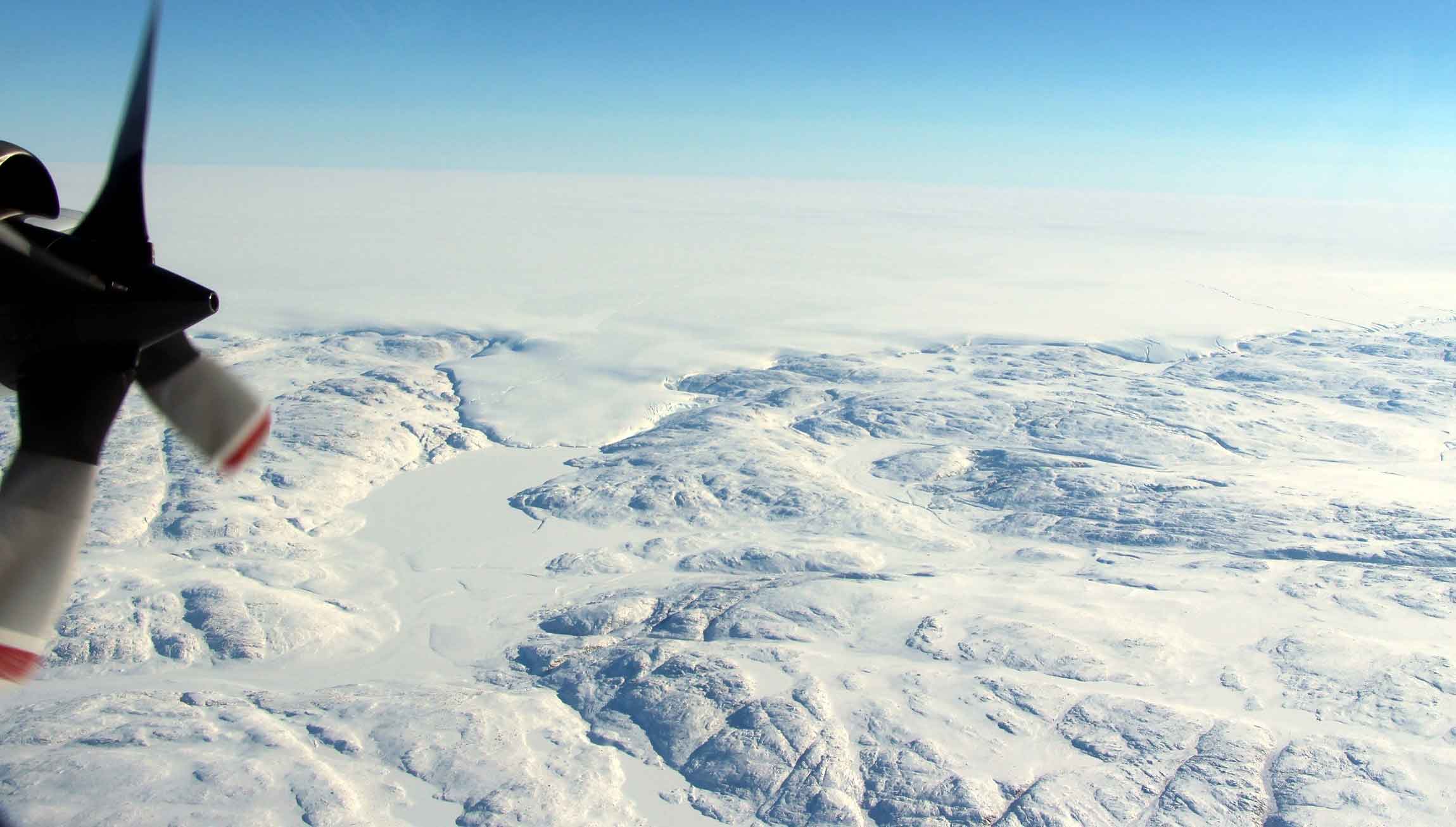 The Hiawatha impact crater is covered by the Greenland Ice Sheet, which flows just beyond the crater rim, forming a semi-circular edge. Part of this edge (top of photo) and a tongue of ice that breaches the crater’s rim are shown in this photo taken during a NASA Operation IceBridge flight on April 17. Credits: NASA/John Sonntag