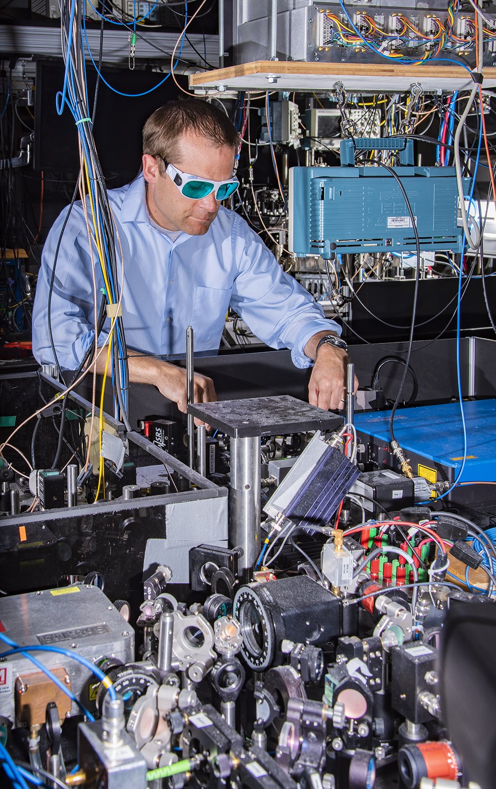 NIST physicist Andrew Ludlow and colleagues achieved new atomic clock performance records in a comparison of two ytterbium optical lattice clocks. Laser systems used in both clocks are visible in the foreground, and the main apparatus for one of the clocks is located behind Ludlow.  Credit: Burrus/NIST