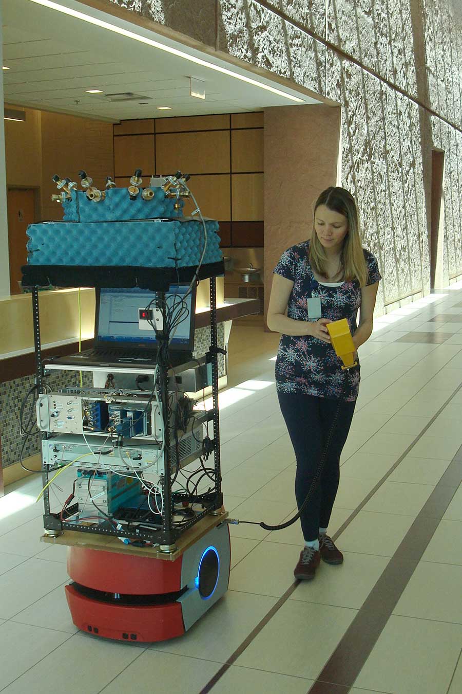 NIST researcher Jelena Senic drives a robot used to measure the performance of different antenna beam patterns. The mobile platform enables researchers to position a wireless channel sounder that includes (top to bottom) an array of 16 receive antennas, the receiver, timing circuitry, a signal digitizer and a battery for untethered field operations. Credit: NIST