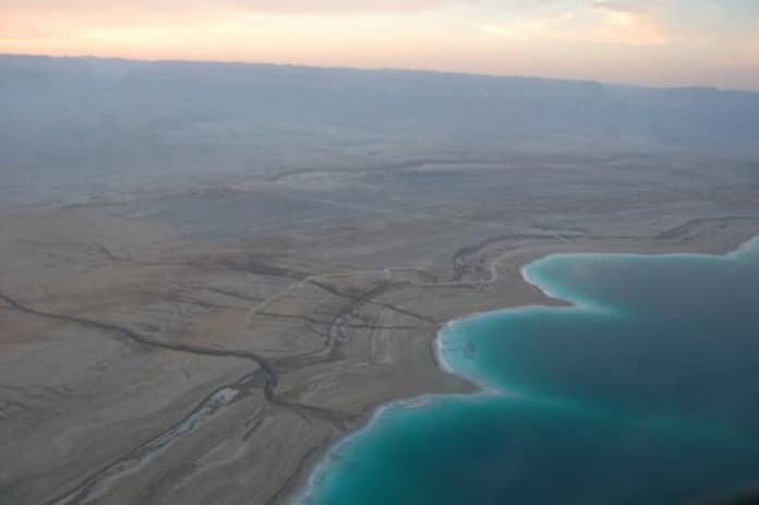 Aerial photograph of the Dead Sea western shore. Parallel paleo shorelines show the intense water level drop (currently about 1 m per year). Salt (halite) actively precipitating from the water column gives this light blue color to the lake. CREDIT Photography courtesy of the International Continental scientific Drilling Program.