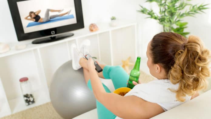 Lazy woman in sport clothing sitting front of the TV and doesn't want to exercise.