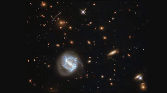 a spiral galaxy (bottom left) in front of a large galaxy cluster
