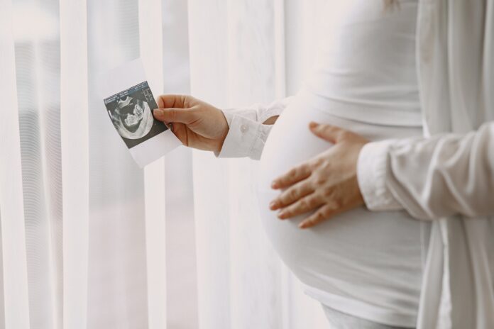 Image showing pregnant woman standing by the window looking at a photo.