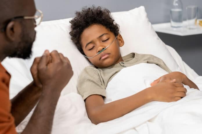 Close-up of African little boy with tube in his nose for breathing sleeping in bed while father visiting to him at hospital