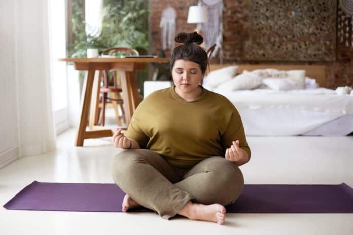 Image showing young chubby female sitting barefooted on yoga mat