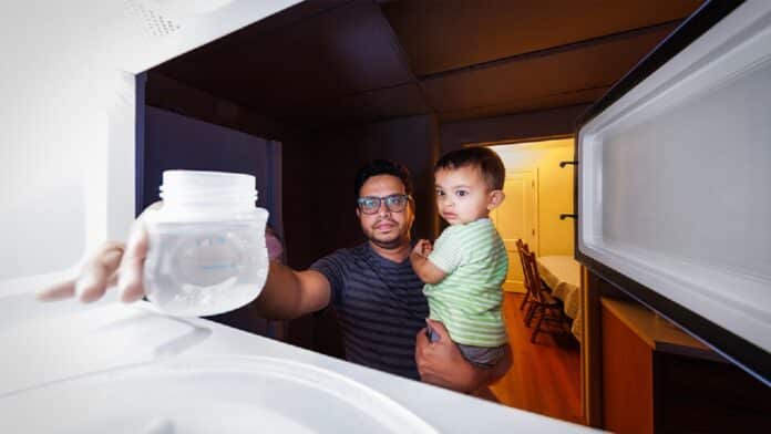 Image showing Kazi Albab Hussain (left) holds his son while removing a plastic container of water from a microwave.