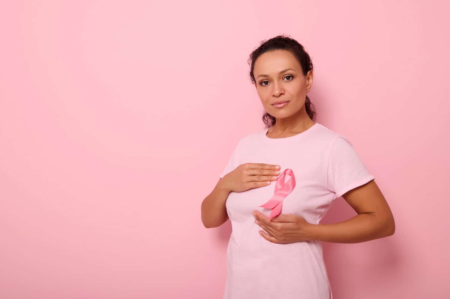 Image showing african american woman puts hands around pink ribbon on her pink t shirt.