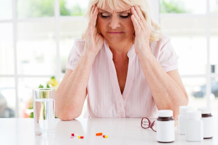 Feeling bad. depressed senior woman holding head in hands and looking at the pills laying on the table