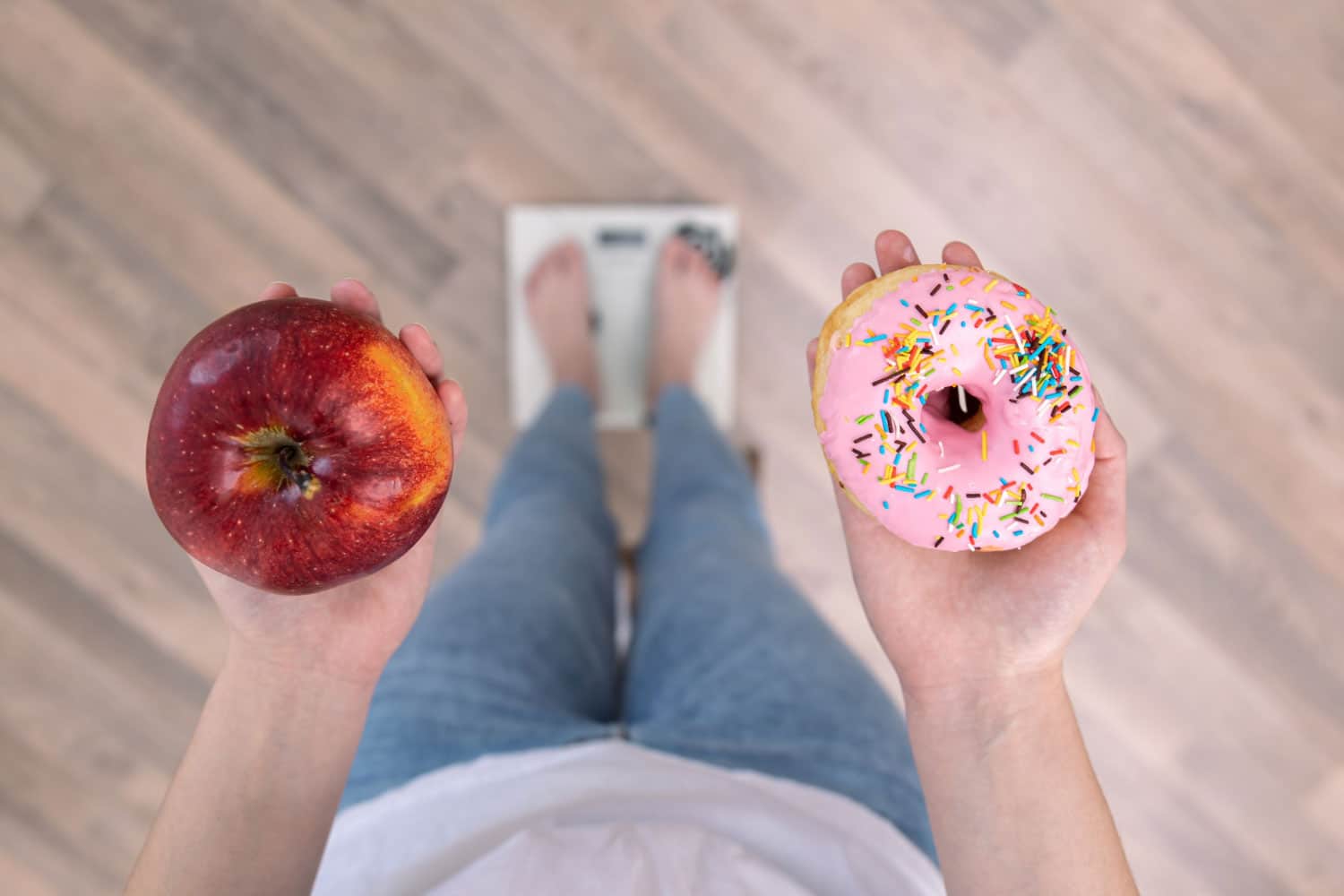 A woman stands on the scales, holds a donut and an apple in her hands, the concept of diet, weight gain, weight loss