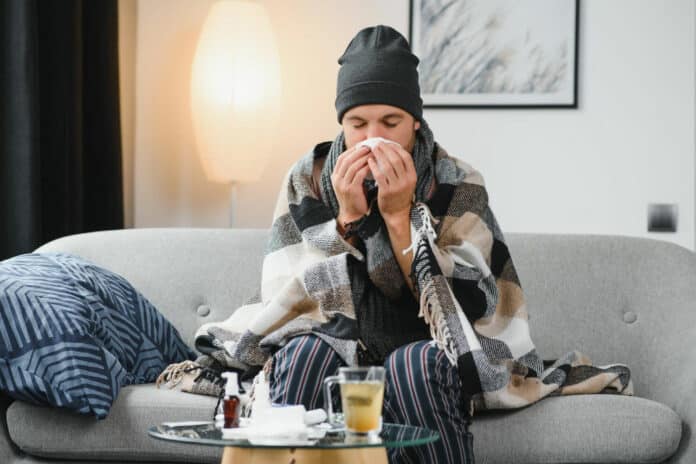 Sick sad man sits on couch at home suffers from runny nose flu