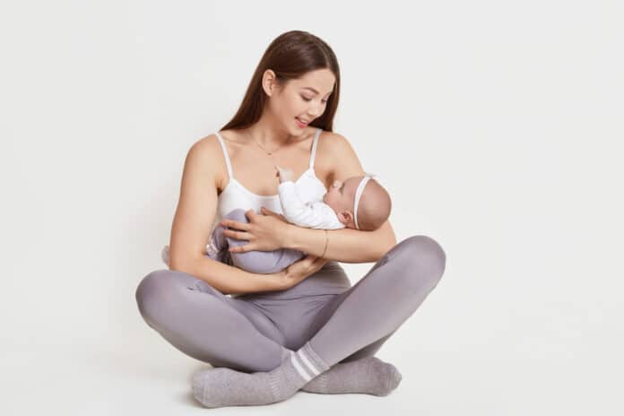 Mother holding newborn baby girl while sitting on floor with crossed legs