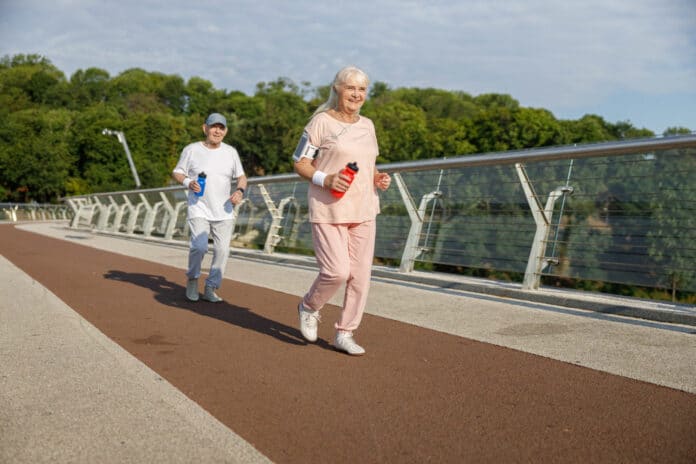Sportive mature woman with friend in tracksuits run training together on modern footbridge