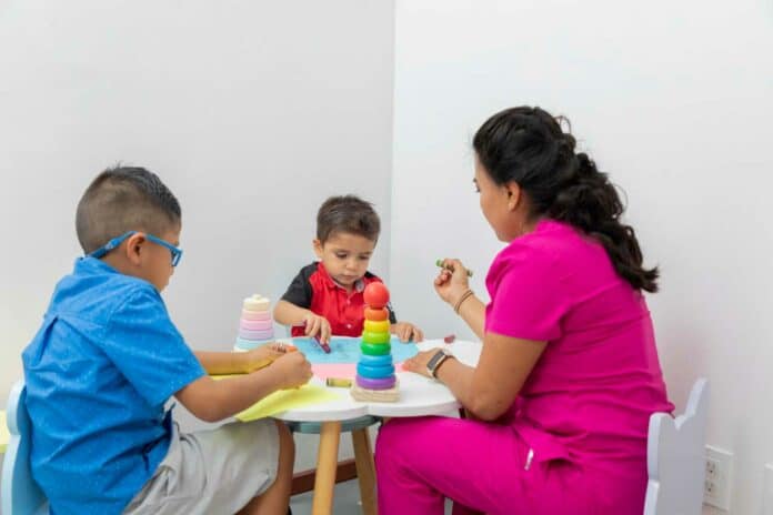 Latina pediatrician doctor playing with two children at a table with toys in her office