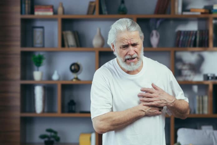 Grayhaired man has severe chest pain grandfather's heart aches holds hands on his chest at home