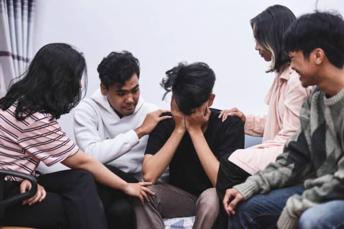 Group of worried friends comforting sad young man who is having problems