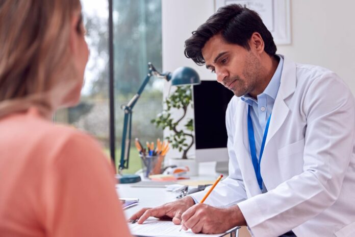 Male doctor or gp meeting mature female patient for appointment in office making notes on clipboard