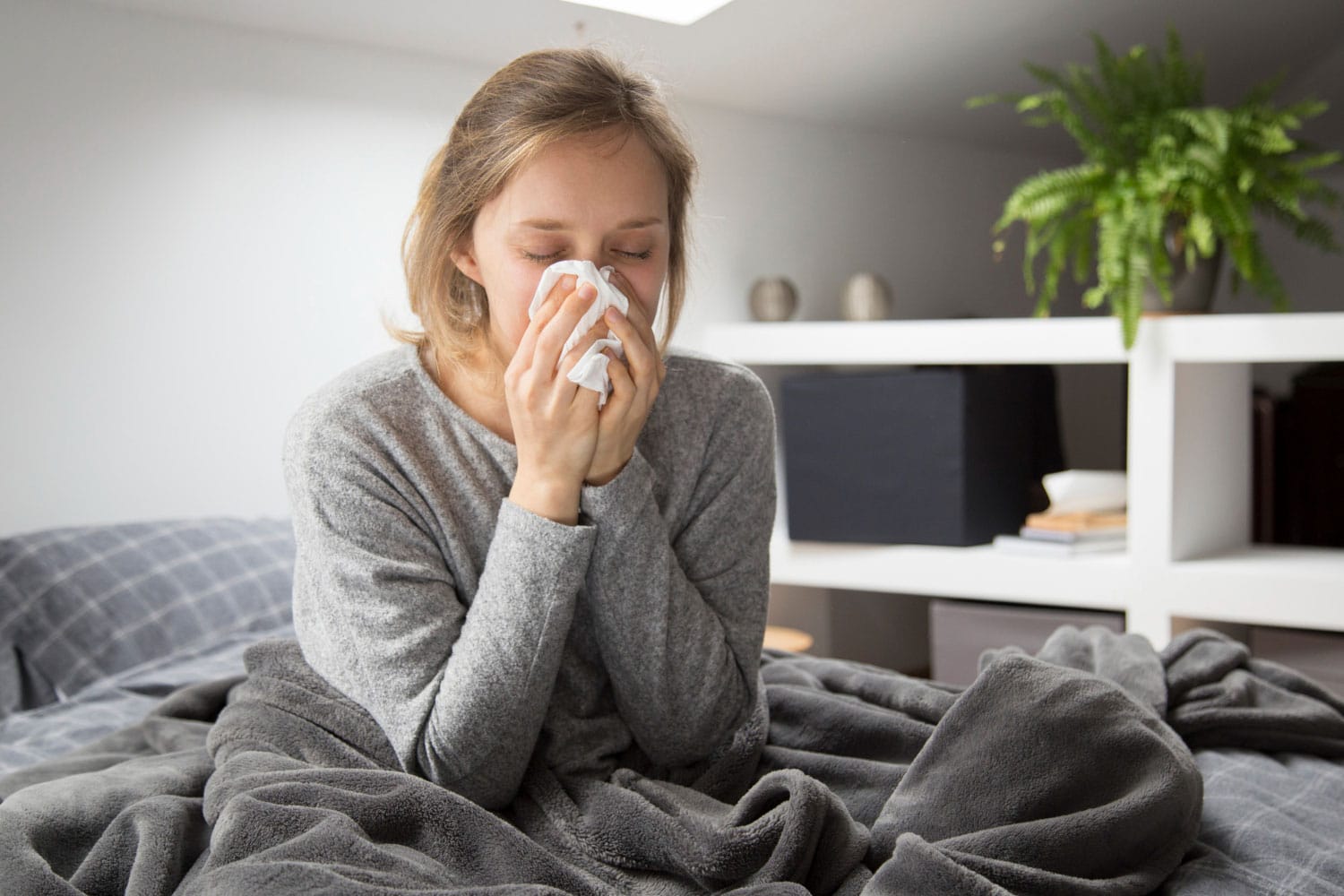 sick woman sitting in bed, blowing nose with napkin
