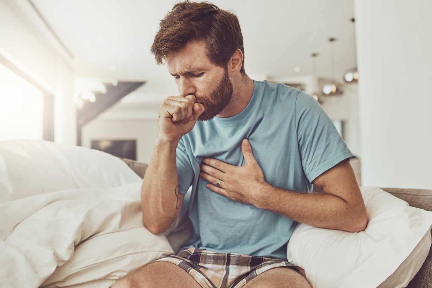 Sick coughing and man on a sofa with chest pain tuberculosis or influenza