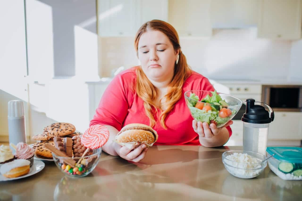 fat young woman in kitchen sitting and eating food.