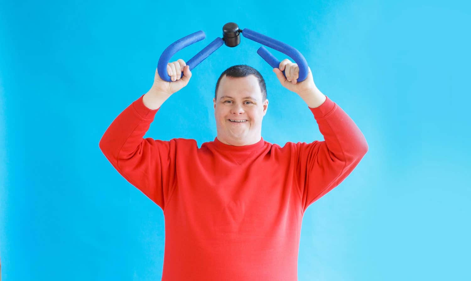 A young man with down syndrome smiles with expanders in his hands