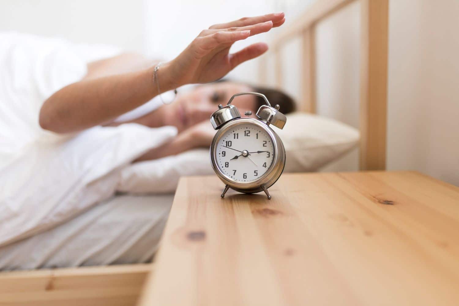 Woman turning off alarm clock while lying on bed