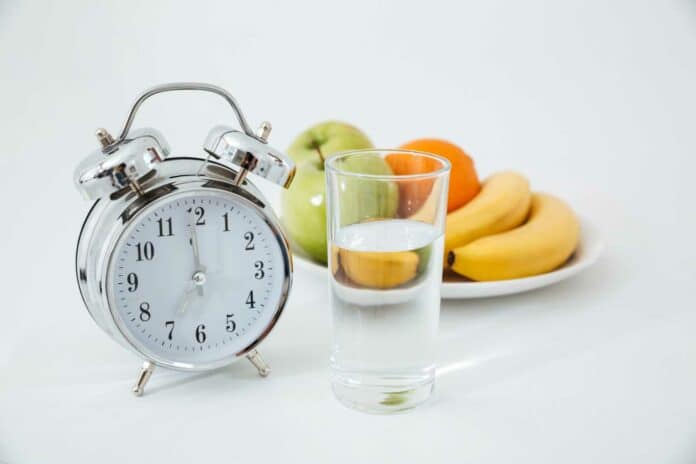 Alarm and glass of water near fruits